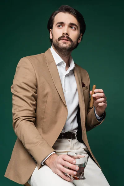 Homme avec moustache tenant cigare et verre de scotch sur vert foncé — Photo de stock