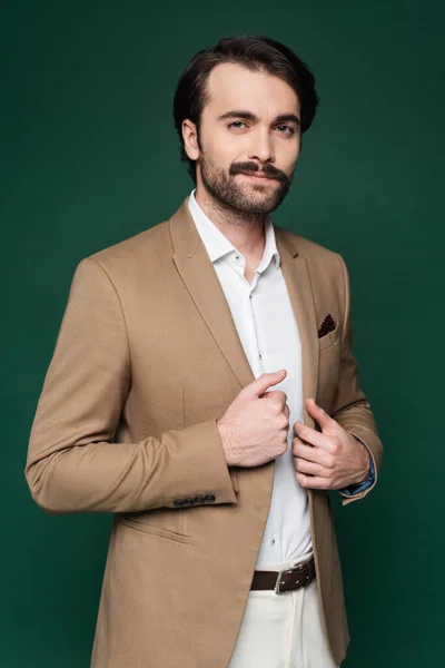 Homme avec moustache ajustant blazer beige sur vert foncé — Photo de stock