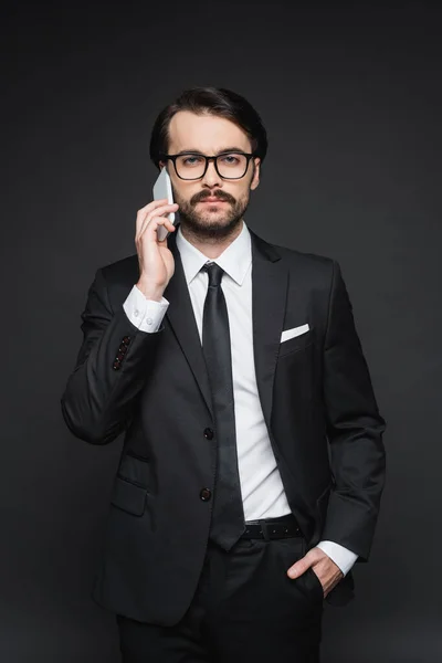 Homme d'affaires en costume et lunettes parlant sur smartphone sur gris foncé — Photo de stock