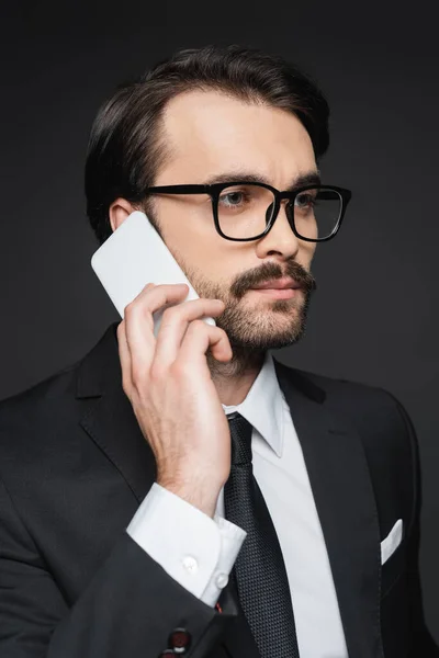 Joven hombre de negocios con bigote hablando en el teléfono inteligente en gris oscuro - foto de stock