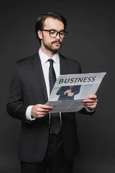 Homme en costume et lunettes lisant journal d'affaires sur gris foncé — Photo de stock