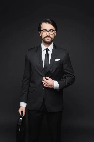 Бізнесмен в костюмі і окулярах тримає шкіряний портфель на темно-сірому — стокове фото