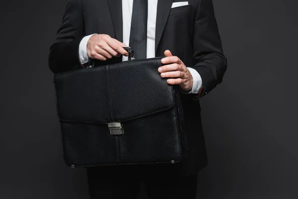 Cropped view of businessman in suit holding leather briefcase on dark grey — Stock Photo