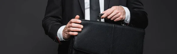 Cropped view of businessman in suit holding leather briefcase on dark grey, banner — Stock Photo