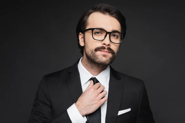 Hombre de negocios con bigote en gafas ajustando corbata en gris oscuro - foto de stock