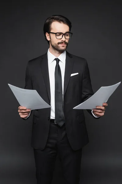 Uomo d'affari con i baffi in occhiali guardando i documenti su grigio scuro — Foto stock