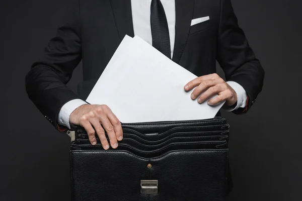 Vue recadrée de l'homme d'affaires mettant des documents dans une mallette en cuir sur gris foncé — Photo de stock