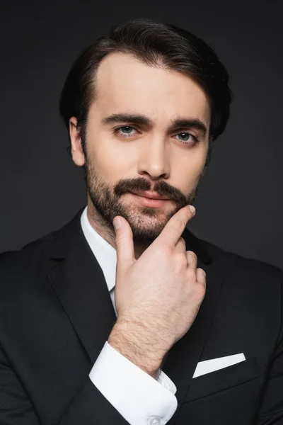 Hombre de negocios pensativo con bigote mirando a la cámara en gris oscuro - foto de stock