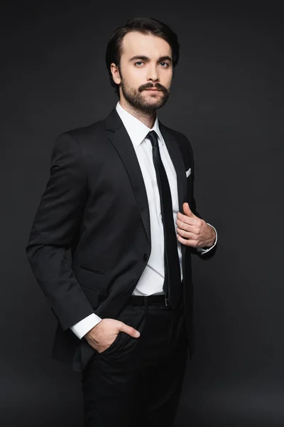 Businessman with mustache looking at camera and posing with hand in pocket on dark grey — Stock Photo