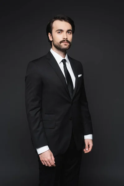 Hombre de negocios con bigote mirando a la cámara mientras está de pie en gris oscuro — Stock Photo