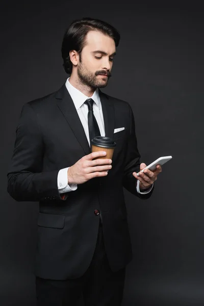 Homme d'affaires avec moustache tenant tasse en papier et smartphone sur gris foncé — Photo de stock