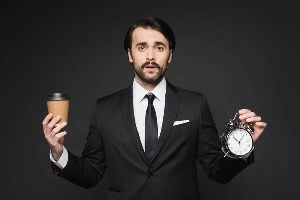 Homme d'affaires avec moustache tenant tasse en papier et réveil sur gris foncé — Photo de stock