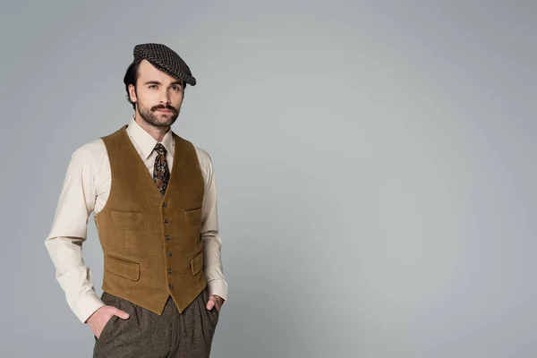 Homem com bigode e roupa retro posando com as mãos nos bolsos em cinza — Fotografia de Stock