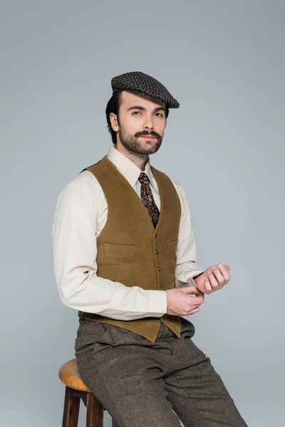 Mann mit Schnurrbart und Retro-Klamotten sitzt auf Stuhl auf grau — Stockfoto