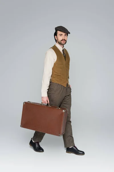 Full length of man with mustache and retro style clothing walking with luggage on grey — Stock Photo