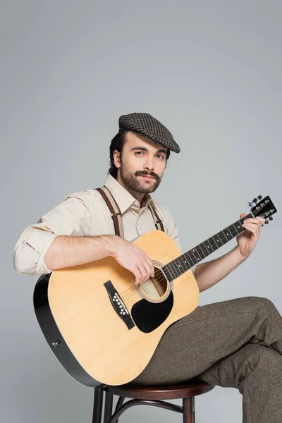 Homem com bigode em roupas de estilo retro e chapéu tocando guitarra acústica isolada em cinza — Fotografia de Stock