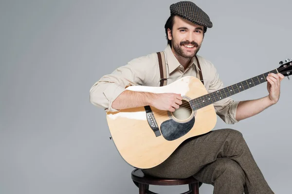 Веселый человек с усами в ретро стиле одежды и шляпы играть акустическую гитару изолированы на сером — стоковое фото