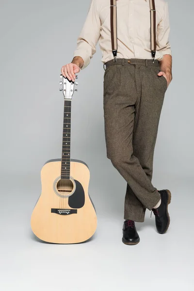 Cropped view of man standing with hand in pocket near acoustic guitar on grey — Stock Photo