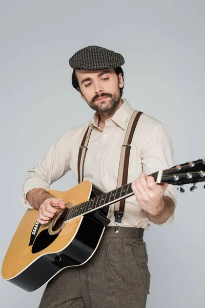 Молодий чоловік з вусами в ретро стилі одягу грає на акустичній гітарі ізольовано на сірому — стокове фото