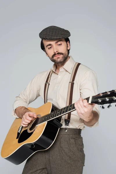 Jovem com bigode em roupas de estilo retro tocando guitarra acústica isolada em cinza — Fotografia de Stock