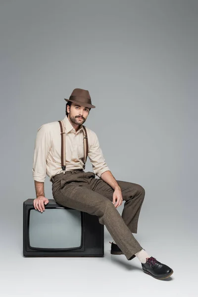 Full length of man retro style clothing sitting on antique tv on grey — Stock Photo