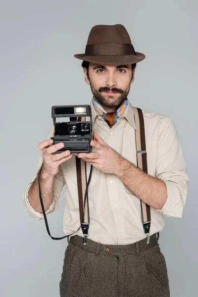 Homme style rétro vêtements et chapeau tenant caméra vintage isolé sur gris — Photo de stock