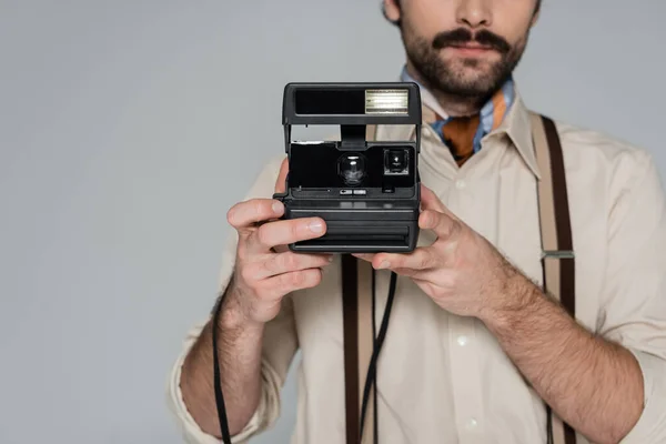 Vista recortada de la ropa de hombre de estilo retro y sombrero que sostiene la cámara vintage aislado en gris - foto de stock