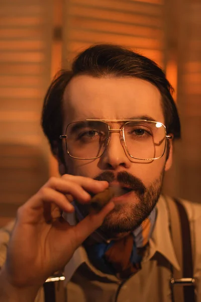 Homem em óculos fumando charuto perto de tela dobrável borrada — Fotografia de Stock