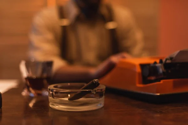 Ashtray with cigar near typewriter machine and blurred man on background — Stock Photo