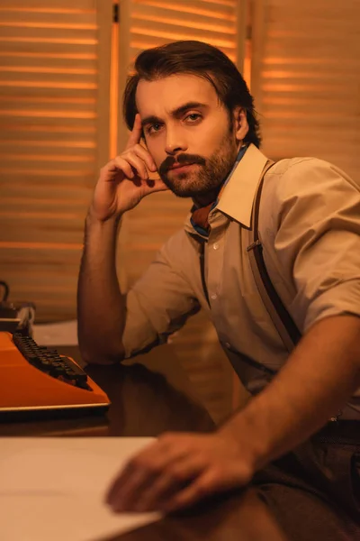 Hombre con bigote cerca de máquina de escribir retro en el escritorio - foto de stock