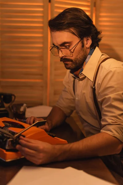 Homem com bigode e óculos olhando para máquina de escrever retro na mesa — Fotografia de Stock