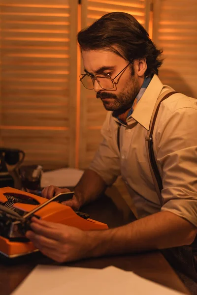 Man with mustache and eyeglasses looking at retro typewriter machine on desk — Stock Photo