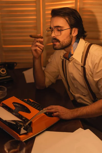 Журналіст з вусами і окулярами курить сигару і дивиться на ретро машинку для друку — стокове фото