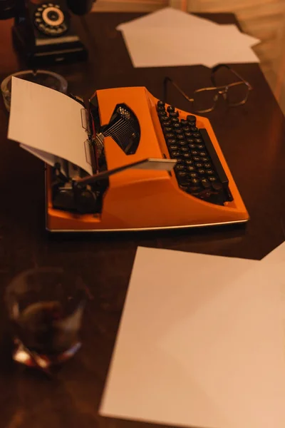 Vista de ángulo alto de la máquina de escribir cerca de papeles y vaso de whisky - foto de stock