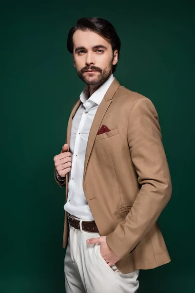 Man in beige blazer looking at camera and standing with hand in pocket on dark green — Stock Photo