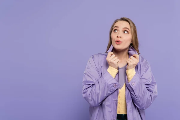Surprised young woman looking away and adjusting collar of trench coat isolated on purple — Stock Photo