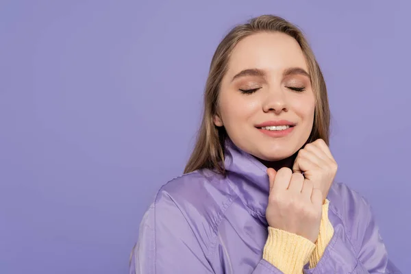 Весела молода жінка з закритими очима в траншеї пальто ізольовано на фіолетовому — стокове фото