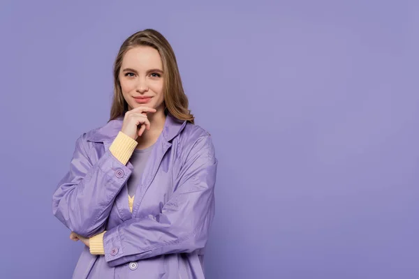 Pleased young woman in trench coat isolated on purple — Stock Photo