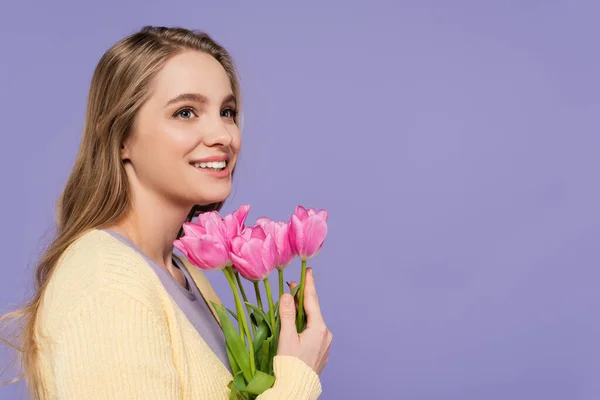 Alegre joven sosteniendo tulipanes rosados aislados en púrpura - foto de stock