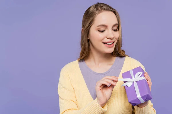 Happy young woman holding wrapped gift box isolated on purple — Stock Photo