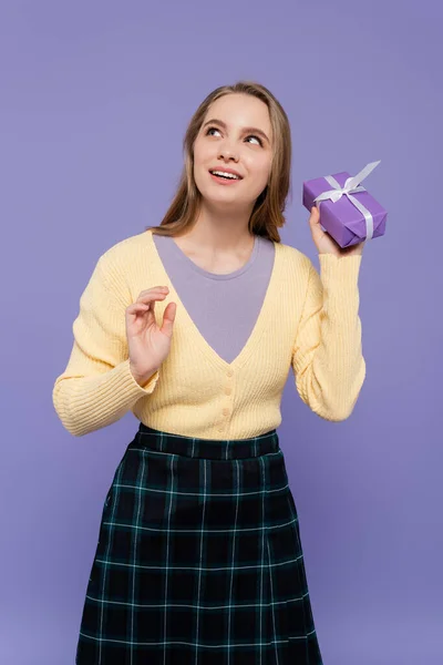 Mujer joven soñadora sosteniendo caja de regalo envuelta aislada en púrpura - foto de stock