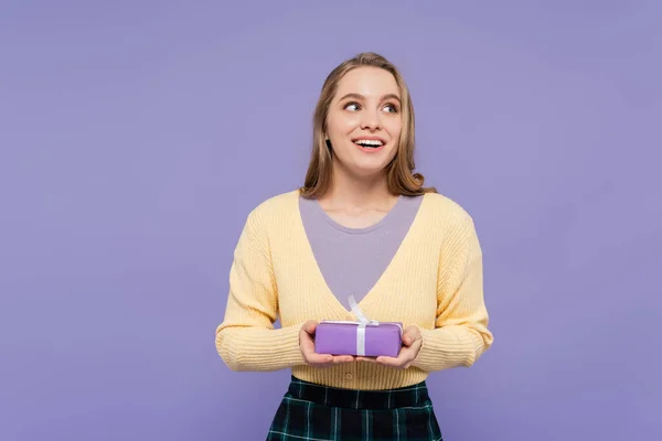 Mujer joven excitada sosteniendo envuelto caja de regalo aislado en púrpura - foto de stock