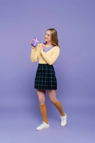 Full length of joyful young woman holding wrapped gift box isolated on purple — Stock Photo