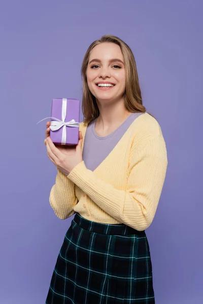 Радостная молодая женщина с упакованной подарочной коробкой изолированы на фиолетовый — стоковое фото