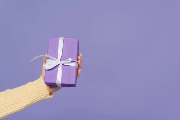 Cropped view of young woman holding wrapped gift box isolated on purple — Stock Photo