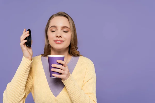 Young woman smelling coffee to go in paper cup isolated on purple — Stock Photo