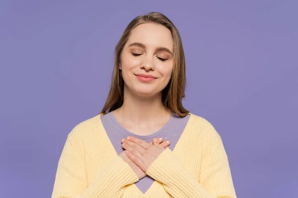 Pleased young woman with closed eyes touching chest isolated on purple — Stock Photo