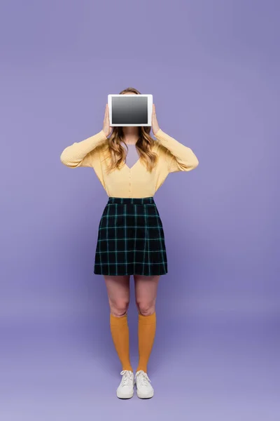 Молода жінка прикриває обличчя, тримаючи цифровий планшет з порожнім екраном на фіолетовому — стокове фото