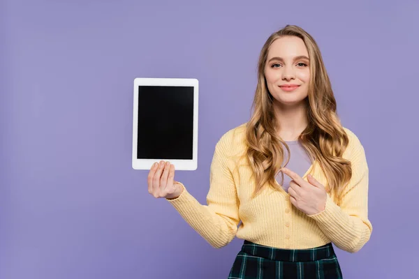 Glückliche junge Frau zeigt auf digitales Tablet mit leerem Bildschirm isoliert auf lila — Stockfoto