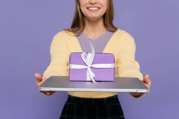 Vista recortada de la joven feliz sosteniendo el ordenador portátil con caja de regalo aislado en púrpura - foto de stock